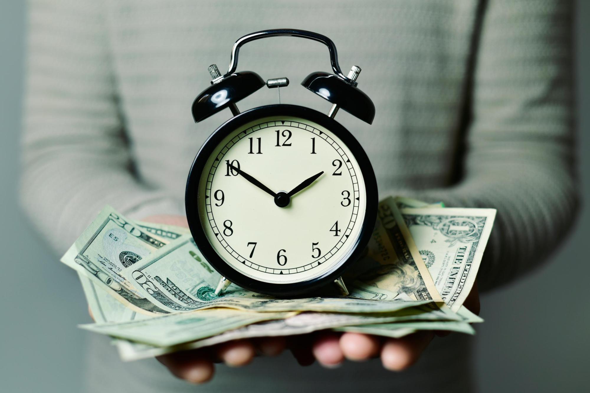 person holding clock with 20 dollar bills underneath