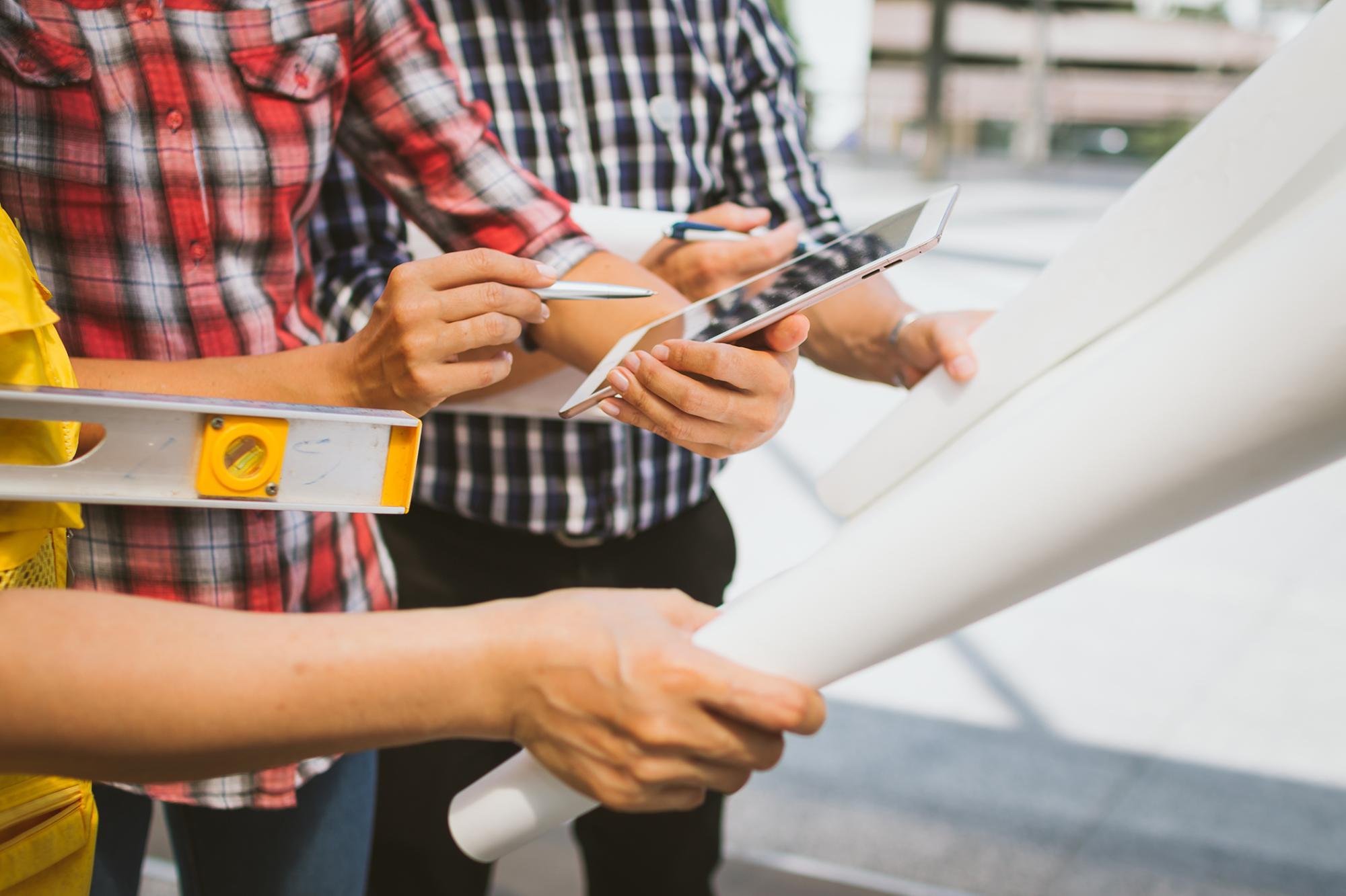 Three contractors analyzing plans on an electronic tablet and paper plans