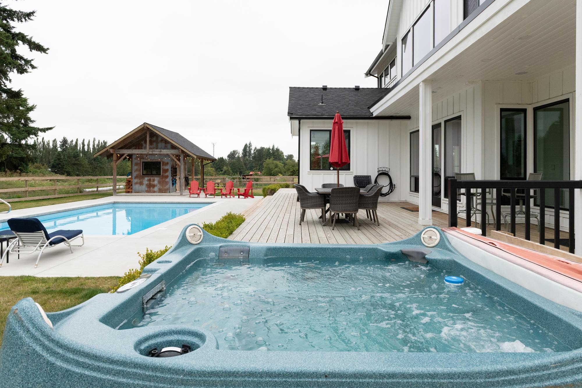 Back yard of home with a hot tub as the focal point and a pool and other small building behind it
